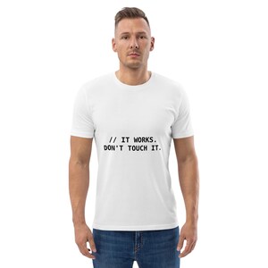Puede incluir: Una camiseta blanca de manga corta con el texto impreso en negro // IT WORKS. DON'T TOUCH IT. centrado en el pecho. La prenda tiene un cuello redondo y un corte estándar, combinada con unos pantalones vaqueros azules.