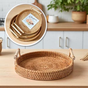 May include: A round, woven rattan tray featuring two light-colored wooden handles on opposite sides. The tray has a textured, circular pattern throughout its base and walls. A small square card with the text Doughnut is placed inside.