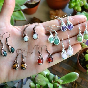 Può includere: Una collezione di orecchini in pietra preziosa fatti a mano. Gli orecchini sono realizzati con filo di rame e presentano varie pietre preziose, tra cui ametista, aventurina verde, occhio di tigre, corniola e giada bianca.