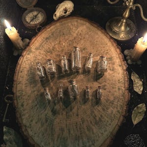 May include: A collection of eleven small, clear glass vials with cork stoppers, each containing a piece of textured, patterned material. The vials are arranged in two rows on a large, oval-shaped wooden slice with visible grain and dark, weathered edges.