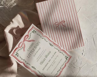 May include: A white baby shower invitation card with red striped backing and a red bow graphic. The front features a scalloped red border with green holly accents and text reading A MERRY LITTLE BABY is on the way! Olivia Grace, Dec. 15.