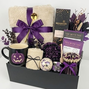 Peut inclure: Un coffret cadeau noir contenant une couverture beige duveteuse avec un ruban violet, une cuillère dorée, un mug noir avec une citrouille violette, un gant de toilette beige, une bombe de bain, un pot de miel, du thé, une cuillère à miel et une bougie violette.