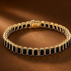 Può includere: Un bracciale color oro caratterizzato da una fila continua di pietre rettangolari nere incastonate in cornici metalliche. Il pezzo include un meccanismo di chiusura a cassetta sicuro che unisce le due estremità, creando una forma circolare.