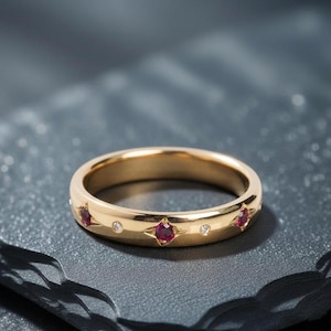 Peut inclure: Une bague en or poli présentant un motif répétitif de rubis rouges ronds et de petits diamants blancs transparents. Les pierres précieuses sont serties dans l'anneau en métal, les rubis étant encadrés par des formes d'étoiles gravées.