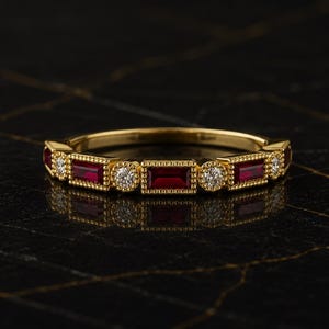 Puede incluir: Un anillo de banda de oro con un patrón alterno de rubíes rojos de corte baguette rectangular y diamantes blancos de corte brillante redondo. Las piedras están engastadas en un marco de oro con detalles milgrain, creando un diseño estructurado.