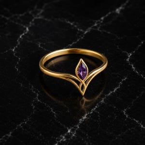 Könnte beinhalten: Ein goldener Ring mit einem violetten Edelstein im Marquise-Schliff, der in ein V-förmiges Band eingefasst ist. Das Metallband hat eine polierte Oberfläche und wölbt sich nach oben, um den zentralen Stein zu halten, was eine spitze Silhouette ergibt.