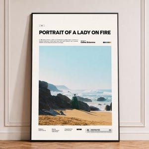 May include: A vertical movie poster for Portrait of a Lady on Fire with a black frame. The design features a central image of a person in a green dress standing on a sandy beach near dark rocks and the ocean, with text details and credits.