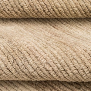 May include: A close-up view of a beige textile featuring a dense, ribbed texture with parallel raised lines running diagonally across the surface. The fabric displays a consistent light tan color with subtle variations in tone throughout the weave.