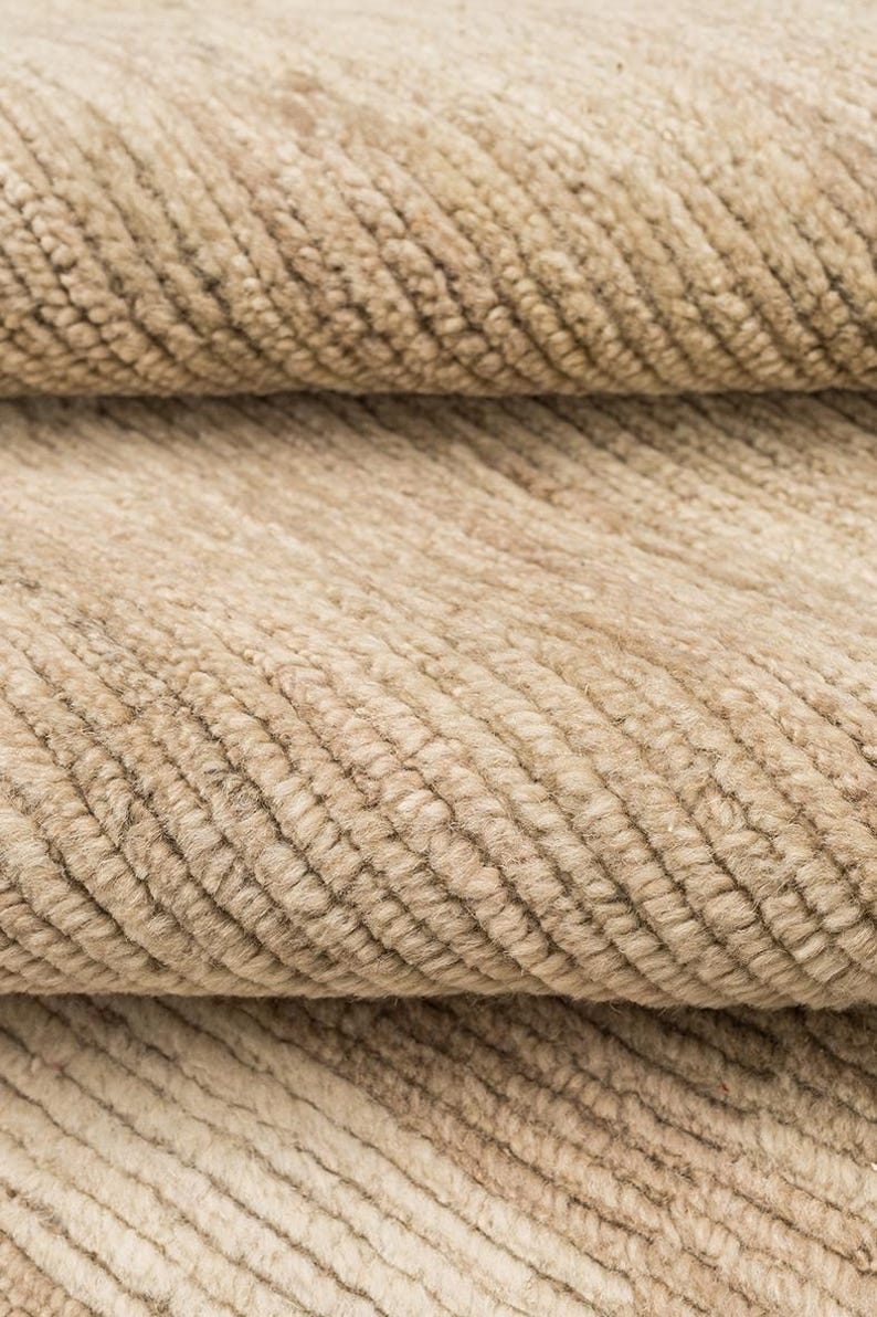 May include: A close-up view of a beige textile featuring a dense, ribbed texture with parallel raised lines running diagonally across the surface. The fabric displays a consistent light tan color with subtle variations in tone throughout the weave.