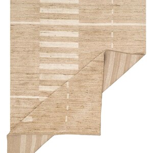May include: A rectangular area rug featuring a woven texture in shades of tan and beige. The design includes a series of horizontal white stripes and a vertical block pattern. One corner of the rug is folded over, revealing a striped underside pattern.