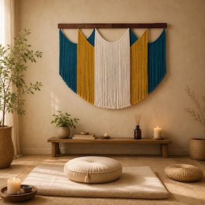 Peut inclure: Une grande tenture murale en macramé composée de longs fils verticaux bleu profond, jaune moutarde et blanc cassé, suspendue à une barre horizontale en bois foncé. L'ouvrage présente un design superposé et incurvé avec une section centrale blanche.