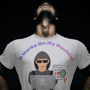 Könnte beinhalten: Ein weißes T-Shirt mit einer Grafik einer Kapuzenfigur, die eine Sonnenbrille und ein Headset trägt und einen Laptop benutzt. Der Text "It Works On My Machine" ist in Lila über der Grafik gedruckt, die auch ein Anmeldefenster und eine Lupe enthält.
