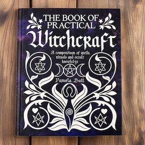 May include: A hardcover book titled The Book of Practical Witchcraft by Pamela Ball. The dark purple and black cover features white decorative floral patterns, geometric symbols, and a central stylized figure with a spiral design.