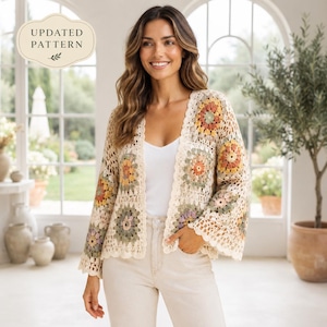 Op de afbeelding: Een crèmekleurig gehaakt vest met een granny square patroon in gedempte tinten saliegroen, oudroze en mosterdgeel. Het vest is aan de voorzijde open, heeft lange, wijde mouwen en een geschulpte rand. Tekst: UPDATED PATTERN.