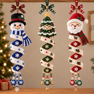 May include: Three hanging crochet ornaments featuring a snowman with a blue scarf, a Christmas tree with a smiling face, and Santa Claus with a red hat. Each ornament has a spiraling tail decorated with snowflakes and dangling beads or bells.