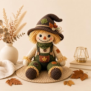 May include: A crocheted scarecrow doll wearing a dark brown hat with a small green patch and orange leaf accents, a green scarf, and dark green overalls with a central orange leaf patch. The doll has yellow yarn hair and a stitched face.