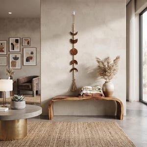 May include: A vertical wall hanging featuring a series of dark brown wooden moon phases carved into crescent and circular shapes, strung together with light-coloured wooden beads and finished with a decorative tassel at the bottom end.