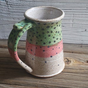 May include: A ceramic mug with a green, pink, and white speckled design. The mug has a large handle.