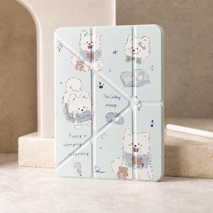 May include: A light blue tablet case featuring a repeating pattern of white fluffy puppies, small brown teddy bears, and blue schoolbags. The text reads The Lukky puppy and Puppy is carrying schoolbag. The case has a geometric folding design.
