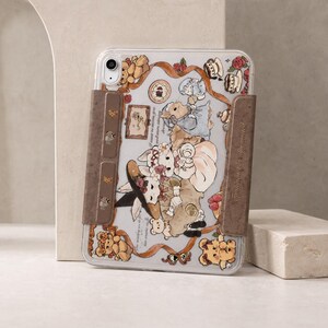 Può includere: Una custodia trasparente per tablet con un'illustrazione di conigli e orsacchiotti antropomorfi in tonalità tenui. La custodia presenta due pannelli laterali marroni con icone di orsetti e il testo To shine not be illuminated.