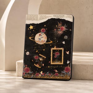 Könnte beinhalten: Eine schwarze E-Reader-Hülle mit einem Himmels- und Blumenmuster, das einen Planeten, Rosen, Schmetterlinge, eine Sanduhr und ein gerahmtes Bild zeigt. Oben ist zeitungartiger Text zu sehen, unten ein goldener Glitzerstreifen mit Rosen.