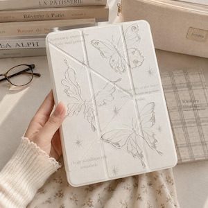 Puede incluir: Una funda para tableta blanca con ilustraciones de mariposas en relieve y detalles de estrellas. La cubierta incluye el texto impreso Romantic proverbs love and poems, The butterfly of the heart only appears in gentle hearts y Daily sunshine via romantic.