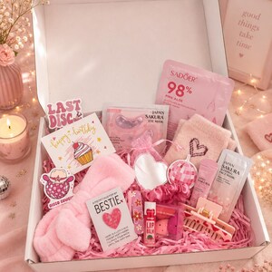 Op de afbeelding: Een geschenkdoos gevuld met roze artikelen, waaronder een pluche hoofdband, pluizige sokken, een Sadoer 98% Pink Aloe gezichtsmasker, Japan Sakura oog- en slaapmaskers, een lippenbalsem, een hartvormige spiegel, een haarklem en diverse stickers.