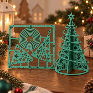 May include: A teal-colored laser-cut wooden Christmas tree set consisting of a flat square panel with two triangular tree cutouts and a spiral design, alongside a three-dimensional conical tree structure featuring intricate holiday motifs.