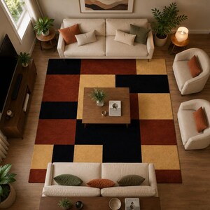 May include: A large rectangular area rug featuring a geometric block pattern in shades of black, burnt orange, and mustard yellow. The rug is positioned in the center of a living room, surrounded by two beige sofas, two armchairs, and a wooden table.