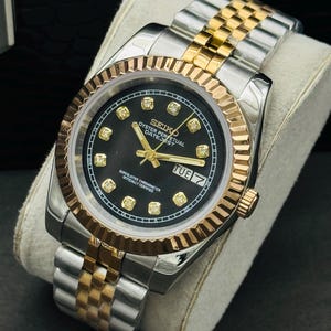 May include: A two-tone Seiko Oyster Perpetual Datejust watch featuring a black dial with gold-tone hour markers set with small clear stones. The watch has a fluted gold-tone bezel, gold-tone hands, and a day-date window at the three o'clock position.