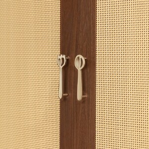 May include: A dark brown wooden cabinet door panel featuring a light beige woven cane texture on both sides. Two silver-toned metal cabinet pulls are mounted vertically, one shaped like a fork and the other shaped like a spoon, centered on the wood.