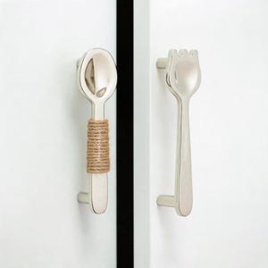 May include: Two silver-toned metal cabinet pulls shaped like kitchen utensils. The left pull is shaped like a spoon with a tan jute rope wrapped around the handle. The right pull is shaped like a fork. Both feature the text CrimsonQuillShop.