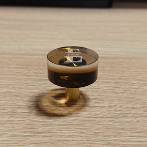 May include: A circular cabinet knob featuring a translucent dark brown resin top with a white engraved letter E and the name Edward. The knob has a polished gold-toned metal base and a cylindrical shape, providing a sleek and functional hardware piece.