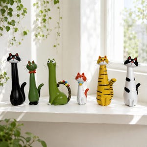 Puede incluir: Una colección de seis figuras de gatos con cuellos alargados y diseños distintos. El conjunto incluye un gato negro sólido, un gato verde con collar rojo, un gato verde con cola rizada, un gato blanco pequeño, un gato atigrado amarillo y un gato blanco con manchas negras.