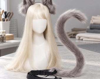 May include: A set of grey faux fur animal ears on a headband and a matching long grey faux fur tail with a black adjustable nylon strap and plastic buckle, displayed on a mannequin head with long straight blonde hair.