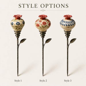 May include: Three decorative garden stakes labeled STYLE OPTIONS, Style 1, Style 2, and Style 3. Each features a bulbous ceramic top with a red floral cap and hand-painted patterns, mounted on a dark, textured metal stem with a single leaf.