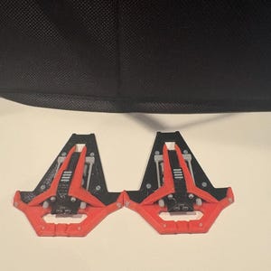 May include: Two identical 3D printed spaceship models featuring a black triangular base, a bright orange outer frame, and grey mechanical details. Each model has a pointed nose, small circular thrusters, and a flat, angular design.