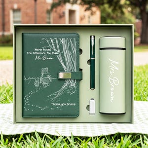 Könnte beinhalten: Ein dunkelgrünes Geschenkset mit einem Notizbuch, einem Stift und einer hellgrünen Isolierflasche. Das Notizbuch zeigt eine weiße Strichzeichnung von Winnie Puuh und Ferkel sowie den Text "Never Forget The Difference You Make Mrs. Brown" und "Thankyou Grace". Die Flasche ist mit "Mrs. Brown" bedruckt.