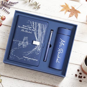 K&ouml;nnte beinhalten: Ein blaues Geschenkset bestehend aus einem Notizbuch, einem Stift und einem Becher. Das Notizbuch zeigt eine wei&szlig;e Strichzeichnung von Winnie Puuh und Ferkel mit dem Text "Never Forget The Difference You Make Mrs. Rachel" und "Thank you Sophia". Der Becher ist mit "Mrs. Rachel" bedruckt.