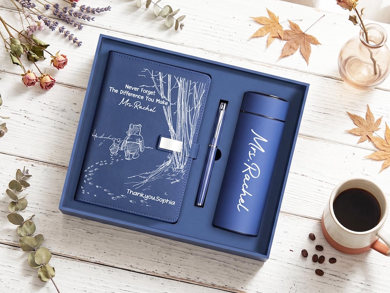 K&ouml;nnte beinhalten: Ein blaues Geschenkset bestehend aus einem Notizbuch, einem Stift und einem Becher. Das Notizbuch zeigt eine wei&szlig;e Strichzeichnung von Winnie Puuh und Ferkel mit dem Text "Never Forget The Difference You Make Mrs. Rachel" und "Thank you Sophia". Der Becher ist mit "Mrs. Rachel" bedruckt.