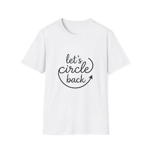 May include: A white short-sleeved t-shirt featuring the black text "let's circle back" printed on the chest. The word "circle" is written in a cursive script, and a curved arrow underlines the text, completing a circular shape around it.