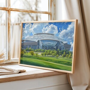 May include: A framed art print featuring a digital painting of a large stadium with a curved glass and metal roof, set against a bright blue sky with white clouds, surrounded by green trees and a grassy field in the foreground.