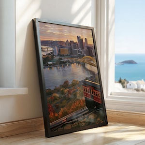 May include: A framed wall art print featuring a scenic view of a city skyline at sunset, with a red funicular car travelling on tracks in the foreground, overlooking a river, a yellow bridge, and urban buildings under a warm, glowing sky.