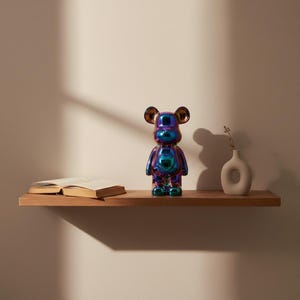 Puede incluir: Una figura con forma de oso con un acabado iridiscente y reflectante que cambia entre tonos azules, morados y verdes. La figura está de pie con orejas redondeadas y una superficie lisa y brillante, situada junto a un libro abierto y un jarrón.