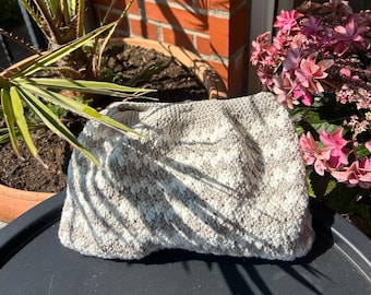 May include: A rectangular crochet clutch bag featuring a textured, variegated pattern in alternating shades of cream and light beige. The surface displays a dense, looped stitch construction with a soft, matte finish and a structured, folded shape.