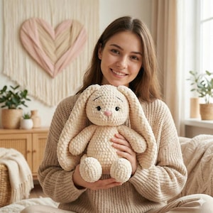 Peut inclure: Un lapin en peluche crocheté de couleur crème avec de longues oreilles tombantes, un petit nez rose et des yeux et sourcils noirs brodés. L'animal en peluche présente une finition en fil texturé doux et est tenu dans un cadre neutre.