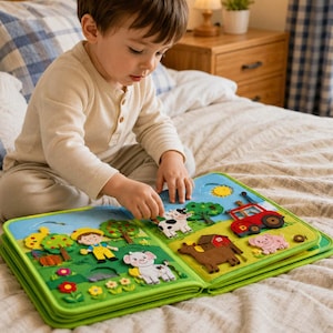 May include: A colorful felt activity book featuring farm-themed scenes with detachable fabric pieces including a farmer, a cow, a pig, a goat, a red tractor, a barn, trees, flowers, and a yellow sun against a bright blue sky background.
