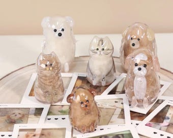 May include: A collection of six small, translucent glass animal figurines, including cats and dogs, arranged on top of several white square photo frames featuring printed images of various pets, all resting on a circular wooden base.