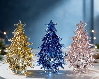 May include: Three glass Christmas tree figurines standing in a row. The left tree is gold, the center tree is deep blue, and the right tree is light pink. Each tree features a pointed star topper and textured, layered branches made of clear glass.