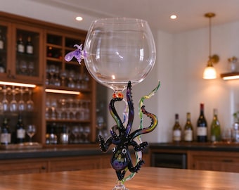 May include: A clear glass goblet featuring a decorative black octopus sculpture wrapped around the stem. The octopus has detailed tentacles and a small purple accent piece attached to the side of the bowl. The base is a standard clear glass disc.